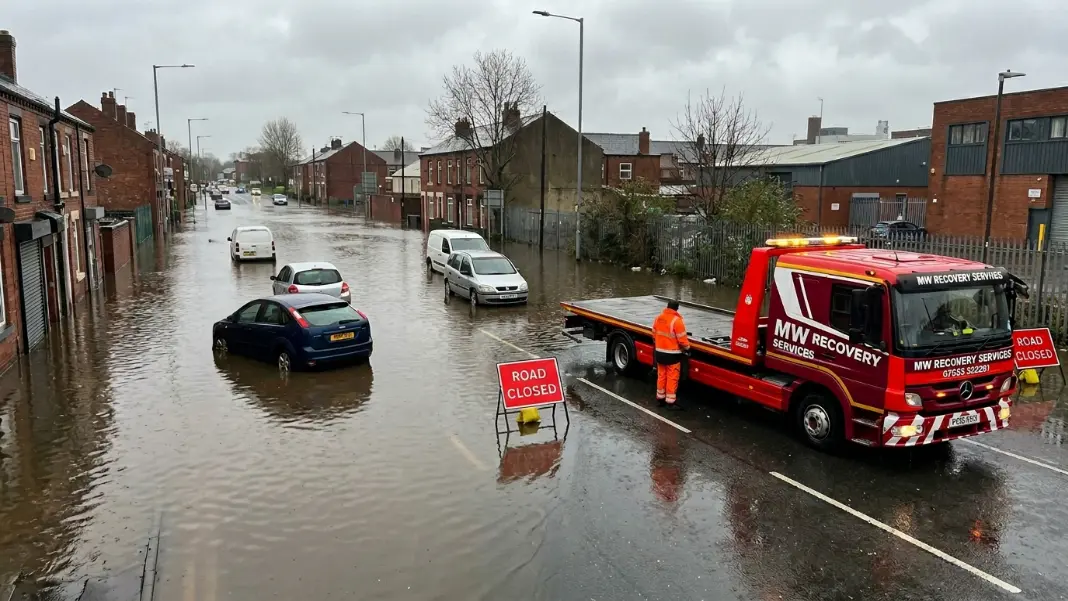 Flooded urban road in Greater Manchester with vehicles abandoned in standing water